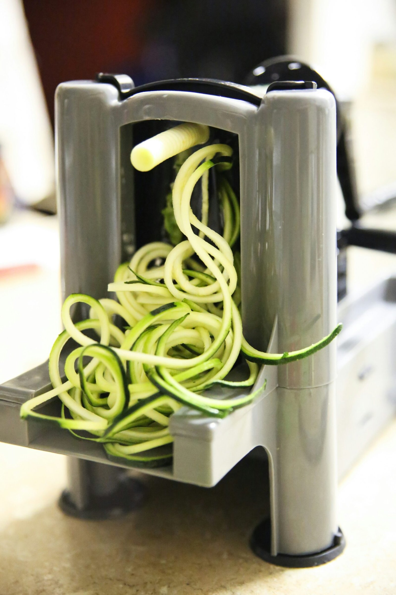 A spiral vegetable slicer creating long, thin zucchini noodles.